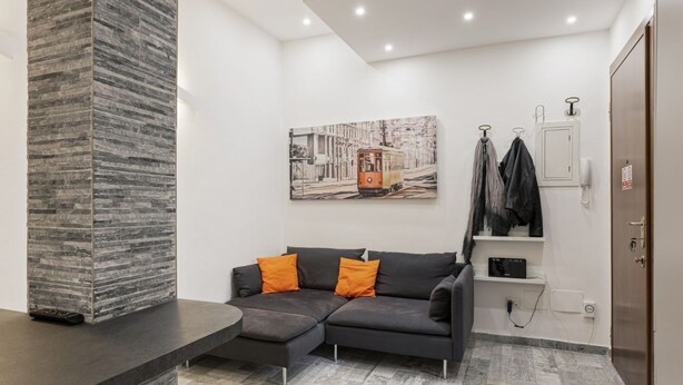 A modern living room with a sectional sofa, a stone accent wall, and a cityscape painting. - Hostmate - Milano - Filzi - Stazione Centrale (Milano)