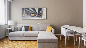 Una sala de estar moderna con un sofá seccional gris, una mesa de comedor con sillas y un cuadro de gran tamaño con un paisaje urbano en la pared.
