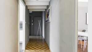 Un pasillo con piso de madera, una puerta blanca y una mesa con sillas, todo en color blanco.