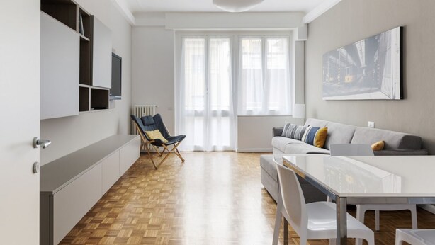 Una sala moderna con un sofá, una mesa de comedor y un televisor montado en la pared.