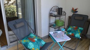 A balcony with two chairs, a small table, and a metal shelf with items. - Air-Conditioned Studio 4 Ppl in Le Grau-du-Roi (Le Grau-du-Roi)
