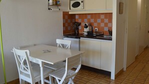 A compact kitchen with a dining table and chairs, a microwave, and a tiled backsplash. - Air-Conditioned Studio 4 Ppl in Le Grau-du-Roi (Le Grau-du-Roi)