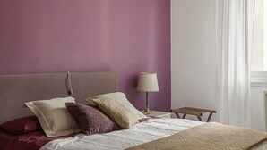 A bedroom with a bed, pillows, a nightstand, a lamp, and a window with curtains. - Hostmate - Milano - Cenisio - Bullona (Milano)