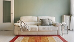 A neutral-colored sofa with a throw blanket and pillows, a patterned rug, and a glass side table with a spherical object. - Hostmate - Milano - Cenisio - Bullona (Milano)