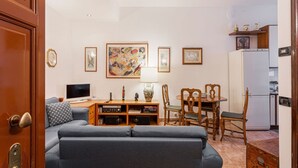 A living room with a sofa, a TV, a table with chairs, and artwork on the wall. - Hostmate - Milano - Via Rovereto (Milano)