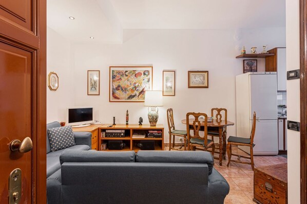 A living room with a sofa, a TV, a table with chairs, and artwork on the wall.