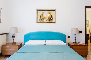 A bedroom with a blue headboard, two bedside tables with lamps, a framed artwork on the wall, and a bed with white pillows.