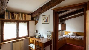 Une pièce avec un bureau en bois, une chaise, un lit, un radiateur et une fenêtre ornée de rideaux en dentelle.