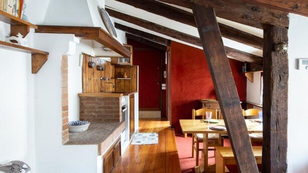 Une cuisine rustique avec des poutres en bois, un mur en briques et un coin repas comprenant une table et des chaises.