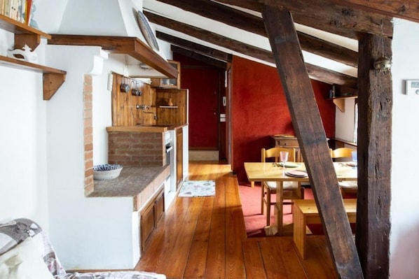 A rustic kitchen with wooden beams, a brick wall, and a dining area with a table and chairs.