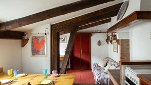 Un coin repas rustique avec des poutres en bois, une porte rouge et une petite cuisine équipée d’une cuisinière.