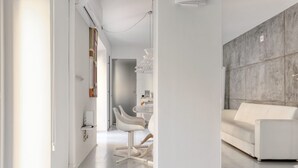 A modern living room with a white sofa, a dining area with white chairs, and a kitchen area with a white countertop.