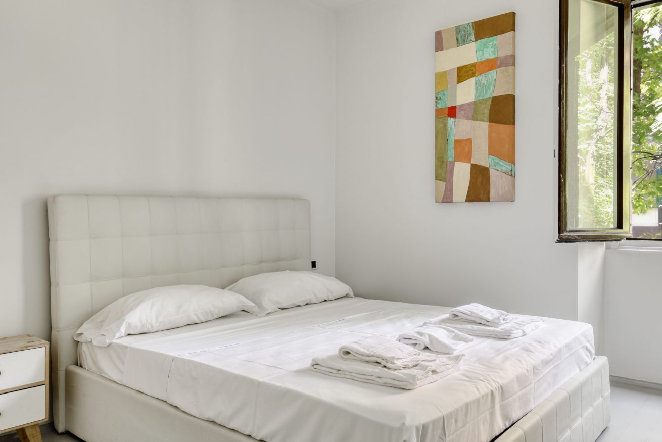 A bedroom with a bed, a nightstand, a window, and a wall art piece.