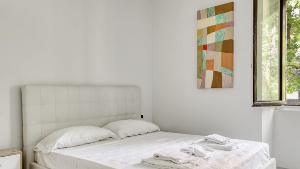A bedroom with a bed, a nightstand, a window, and a wall art piece.