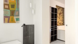 A hallway with a white wall, a geometric artwork, a black door, and a patterned wall.