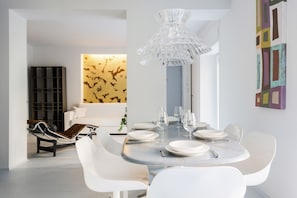 A dining area with a round table set for six, white chairs, and a modern chandelier. - Hostmate - Milano - Solferino - Brera (Milano)
