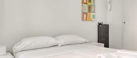 Una cama bien hecha con ropa de cama blanca, una mesita de noche con lámpara y una obra de arte colgada en la pared.