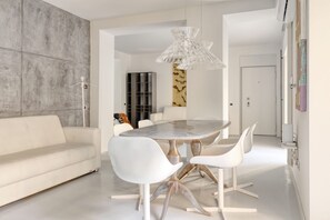 A modern dining area with a round table, white chairs, and a unique chandelier.