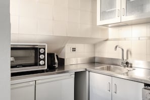 A compact kitchen with a built-in microwave, a coffee maker, a stainless steel sink, and white cabinetry. - Hostmate - Milano - Solferino - Brera (Milano)