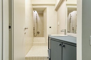 A bathroom with a tiled floor, a sink, a mirror, and a shower.