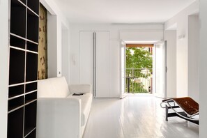 A modern interior with a white sofa, a metal-framed chair, and a view through an open door to an outdoor balcony.