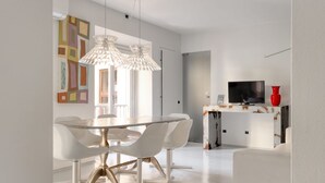A modern dining area with a white table and chairs, pendant lights, and a television on a white console.