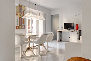 A modern dining area with a white table and chairs, pendant lights, and a television on a white console. - Hostmate - Milano - Solferino - Brera (Milano)