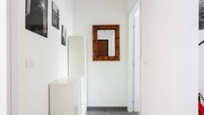 Ein schmaler Flur mit einem spiegelnden Wandbild aus Holz, einer weißen Tür am Ende und einem Lichtschalter links.