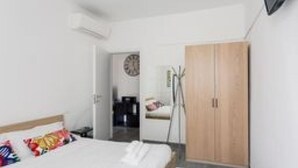Ein Hotelzimmer mit einem Bett, einem Holzschrank, einem Schreibtisch mit Stuhl und einer Wanduhr.