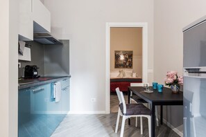 A compact kitchen with modern appliances, a dining area with a table and chairs, and a painting on the wall.