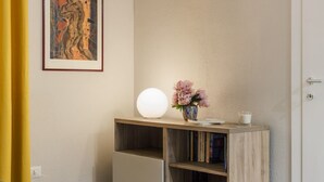 Una stanza con un tavolo consolle in legno, un vaso con fiori, una lampada sferica bianca e un quadro appeso al muro.