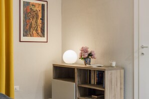 A room with a wooden console table, a vase with flowers, a white spherical lamp, and a framed painting on the wall.