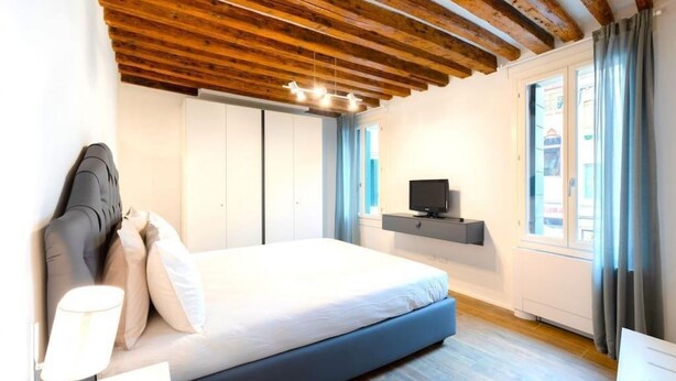 Una camera da letto con un letto, una TV, una scrivania e una finestra con tende.