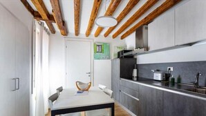 Una cucina moderna con travi in legno, un tavolo da pranzo con sedie e vista su uno spazio verde esterno.