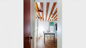 Un corridoio con travi in legno, una sala da pranzo con tavolo e sedie, e una porta che dà su un'altra stanza.