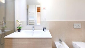 Un bagno moderno con un ampio lavandino bianco, uno specchio e una doccia.