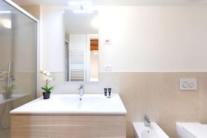 A modern bathroom with a large white sink, a mirror, and a shower.