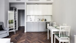 A compact kitchen with white cabinets, a dining table, and a gray sofa. - Hostmate - Milano - Freguglia's Studio - Guastalla (Milano)