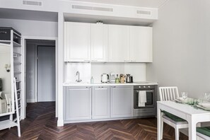 Ett modernt kök med vita skåp, en inbyggd ugn och en matplats med ett vitt bord och stolar.