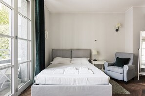 A bedroom with a bed, a chair, a nightstand, and a window. - Hostmate - Milano - Freguglia's Studio - Guastalla (Milano)