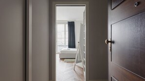 A hallway with a wooden door, a white bench, and a view into a room with a window and curtains. - Hostmate - Milano - Freguglia's Studio - Guastalla (Milano)