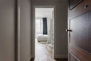 En hall med en trädörr, en vit bänk och utsikt in i ett rum med ett fönster och gardiner.