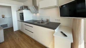 Een moderne keuken met witte kasten, een zwart aanrecht, een inbouwoven en een wandtelevisie.