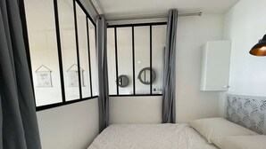 Een slaapkamer met een bed, een raam met gordijnen, een nachtkastje en een wandlamp.