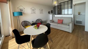 Een moderne woonkamer met een ronde eettafel, zwarte stoelen, een grijze bank met een rode kussen, en een hangende lamp.