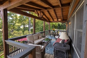 A covered outdoor area with a wooden ceiling, wicker furniture, and a view of greenery.
