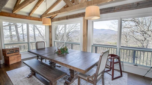 Une salle à manger rustique avec une grande table en bois, des bancs et une vue sur un paysage montagneux grâce à de grandes fenêtres.