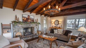 Un salon chaleureux avec une cheminée en pierre, des poutres en bois, une grande horloge et un lustre de style rustique.