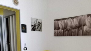 A room with a bed, a small desk, a chair, a wall-mounted telephone, and a door. - Apartment Roberto  (Gallipoli)