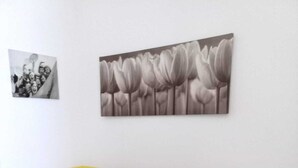 A grey and white sofa against a yellow wall, with a black and white photograph and a floral painting above it. - Apartment Roberto  (Gallipoli)